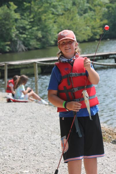 Boy wearing life jacket by lake with fishing pole